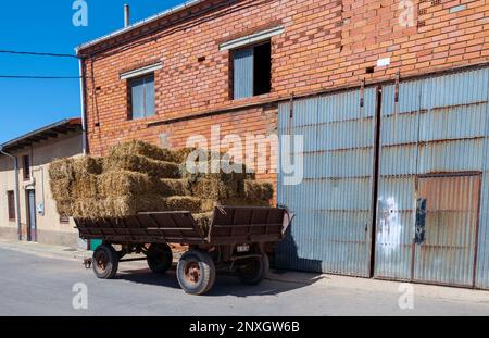 Vieille remorque de tracteur empilée avec des balles de foin de paille dans la rue dans un village espagnol Banque D'Images