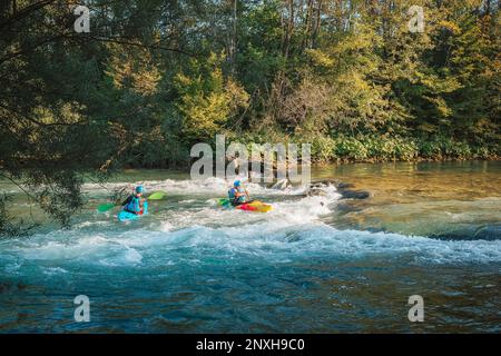 Deux kayakistes pagayant et manœuvrant sur la rivière à mouvement rapide avec une rive rocheuse et allant sous le pont de béton Banque D'Images