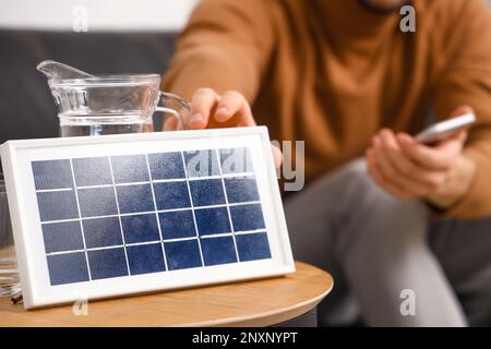 Jeune homme avec téléphone portable près du panneau solaire portable à la maison, gros plan Banque D'Images