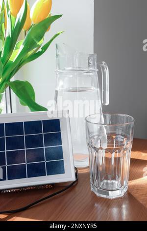 Panneau solaire portable, verseuse d'eau et vase avec tulipes sur la table près de la fenêtre, gros plan Banque D'Images