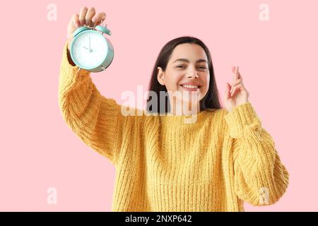 Belle jeune femme avec réveil croisant les doigts sur fond rose Banque D'Images