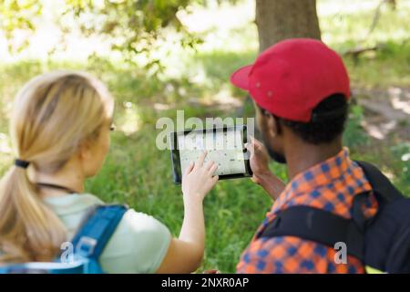 Vue arrière de divers couples en randonnée dans une forêt ensoleillée, en vérifiant la carte gps sur une tablette Banque D'Images