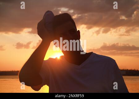 Homme avec sac froid souffrant de coup de chaleur à l'extérieur au coucher du soleil Banque D'Images