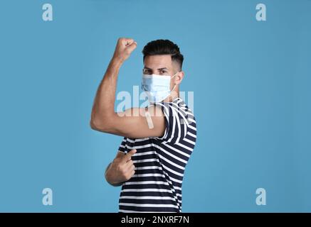 Homme vacciné avec masque de protection montrant du plâtre médical sur son bras sur fond bleu clair Banque D'Images