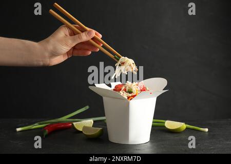 Femme mangeant des nouilles wok végétariennes avec des baguettes de la boîte à table noire, en gros plan Banque D'Images