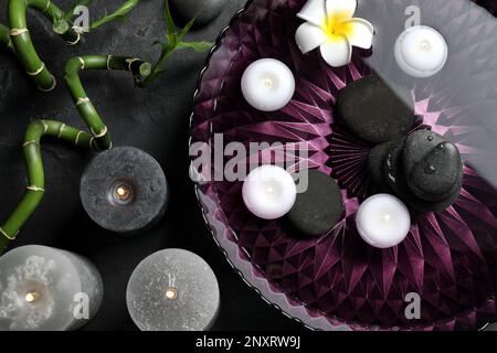 Composition de pose plate avec bougies allumées et pierres spa sur table noire Banque D'Images