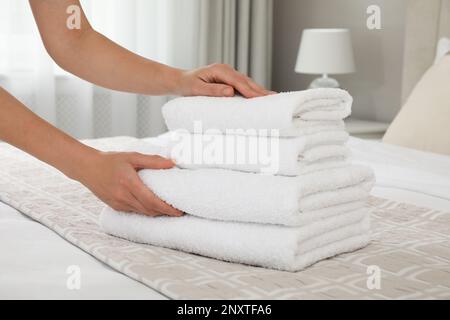 Femme mettant des serviettes propres sur le lit dans la chambre, gros plan Banque D'Images