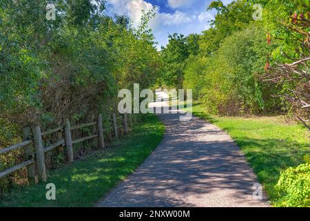 Longue route le long du parc, séparée par une clôture de poteaux ronds en bois Banque D'Images