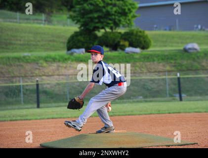 Un jeune lanceur de baseball est pris dans l'action de piller le baseball pendant un match au Tennessee. Il porte un uniforme gris, bleu et rouge. Banque D'Images