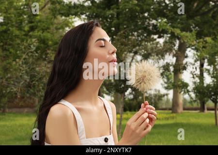 Belle jeune femme soufflant grand pissenlit dans le parc. Concept anti-allergie Banque D'Images