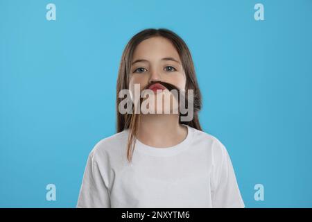 Jolie petite fille qui fait de la fausse moustache avec ses cheveux sur fond turquoise Banque D'Images