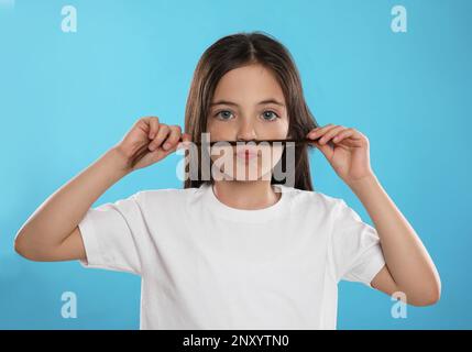 Jolie petite fille qui fait de la fausse moustache avec ses cheveux sur fond turquoise Banque D'Images