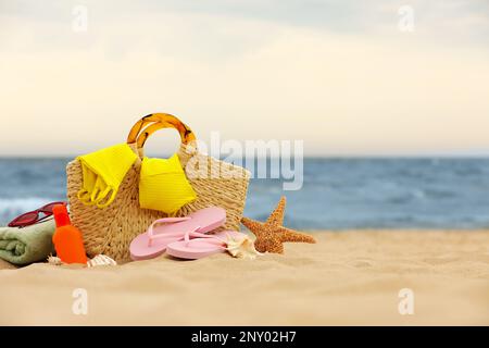 Sac et différents objets de plage sur le sable près de la mer, espace pour le texte Banque D'Images