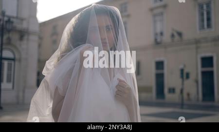 Belle femme avec voile blanc en ville. Action. Mariée en voile blanc pose dans la vieille ville. Femme avec voile sur la rue de la ville le jour ensoleillé d'été. Banque D'Images