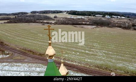 Hiver initial. Clip.View d'un drone sur un paysage avec de l'herbe neigeuse dans un champ où il y a un temple avec une croix dorée sur un dôme doré contre Banque D'Images