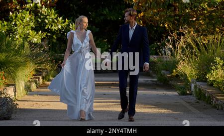 Jeunes mariés marchant dans le parc. Action.Une belle mariée blonde dans une robe blanche avec des talons avec son marié barbu dans un costume noir tenant han Banque D'Images