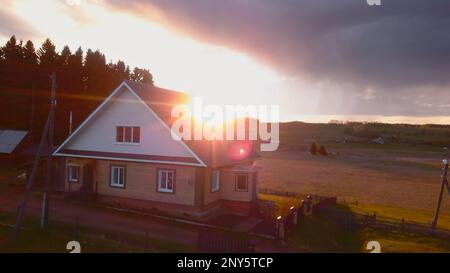 Le beau soleil de l'aube brille sur un paysage rustique en été. Attache. Maison dans le village sur fond de soleil lumineux de l'aube. Paysage d'été rustique avec maison a Banque D'Images