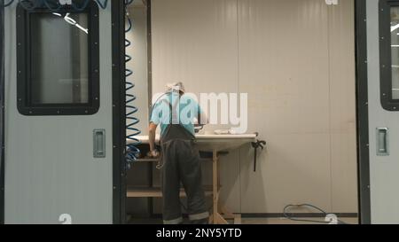 Le travailleur polit les panneaux en bois. Créatif. Vue arrière du travailleur dans les planches à polir. Polissage des planches dans une entreprise de travail du bois. Banque D'Images