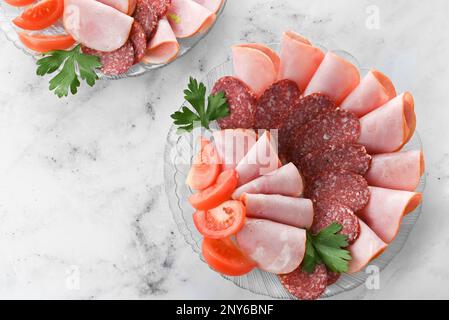 assiette avec un assortiment de saucisses cuites fumées sur une table lumineuse. Charcuterie de saucisses aux herbes et légumes Banque D'Images