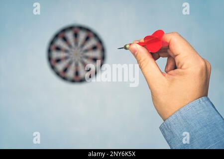 Dart rouge dans l'homme de main de point cible sur le mur bleu, selective focus on cible dart, concept de gagner. une main d'homme lance une fléchette sur la cible. Banque D'Images