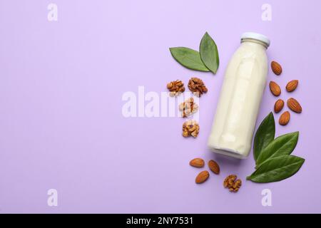 Bouteille de lait végétalien, noix et amandes sur fond violet, plat. Espace pour le texte Banque D'Images