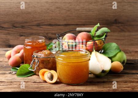 Pots avec différents confitures et fruits frais sur table en bois Banque D'Images