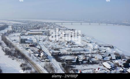 Vue aérienne d'une zone industrielle enneigée de la ville. Attache. Vol au-dessus de la ville blanche d'hiver avec la rivière et le pont en arrière-plan Banque D'Images
