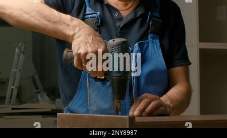 Gros plan d'un menuisier à l'aide d'un tournevis tout en travaillant avec un produit en bois. Créatif. Travaux de bois à l'atelier Banque D'Images