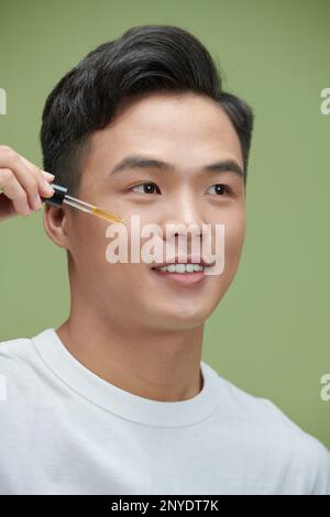 Jeune homme appliquant du sérum organique essentiel sur le visage à l'aide d'une pipette Banque D'Images