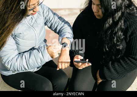 deux belles femmes latines de cheveux longs synchronisant les données sur le smartphone et la montre intelligente, shopping sur le net, internet shopping concept Banque D'Images