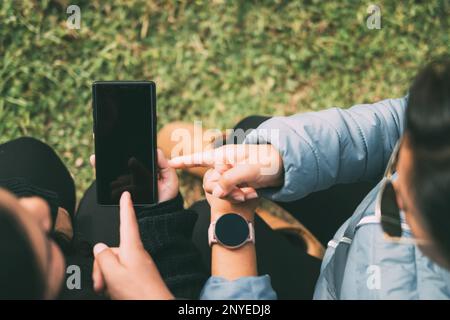 Les mains rognées d'une femme avec une montre intelligente, pointant vers un smartphone, le concept de technologie, les réseaux sociaux, avec deux personnes indiquant quelque chose Banque D'Images