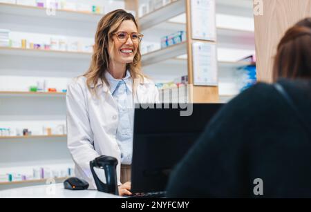 Une pharmacienne aide un patient en vente libre dans un magasin de médicaments. Un professionnel de la santé amical qui distribue des médicaments dans une pharmacie. Banque D'Images