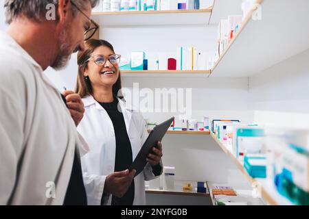 Les pharmaciens hommes et femmes travaillent ensemble dans un chimiste. Deux professionnels de la santé matures faisant un inventaire prennent dans une pharmacie. Banque D'Images