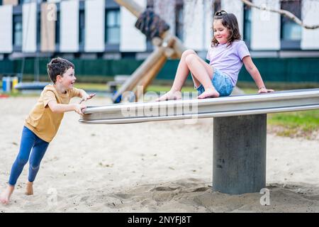 Ensemble complet d'enfants positifs dans des tenues décontractées d'été souriant tout en jouant sur le terrain de jeu et en s'amusant ensemble pendant le week-end Banque D'Images