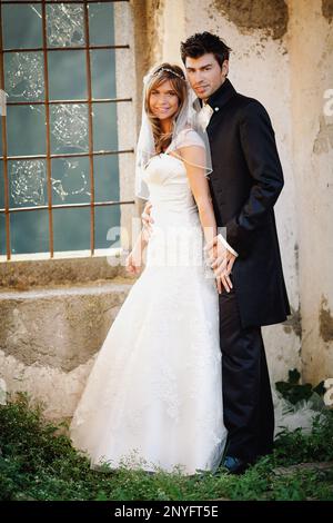 Homme attrayant en costume élégant et jolie femme en blanc habillez-vous en souriant et regardez l'appareil photo tout en vous tenant près du vieux bâtiment Banque D'Images