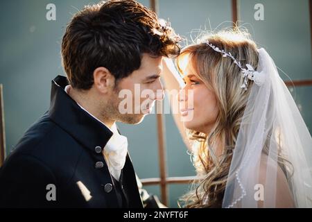 Homme attrayant en costume élégant et jolie femme en blanc habillez-vous en souriant et regardez les uns les autres tout en vous tenant à proximité bâtiment vieillissant Banque D'Images