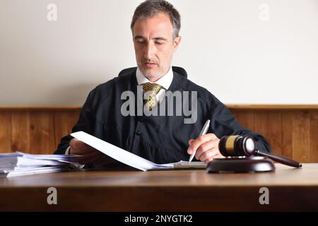 Un juge assis dans un fauteuil examine le résumé d'une affaire sur une table en bois. Vue avant Banque D'Images