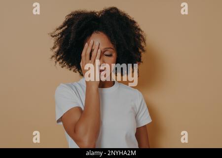 Photo studio de jeune femme bouleversée de race mixte frustrée par des problèmes dans la vie ou les relations, couvrant le visage avec la main et se sentant l'anxiété ou le déprr Banque D'Images