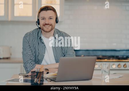 Beau homme heureux responsable de l'assistance clientèle donne des conseils ou de la consultation aux clients travaille en ligne à partir de poses à la maison à la cuisine porte sans fil hepho Banque D'Images