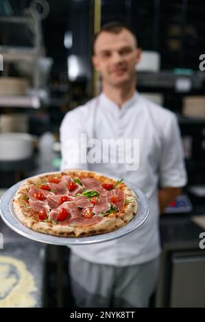 Portrait d'un pizzéiolo masculin présentant une pizza fraîchement cuite Banque D'Images