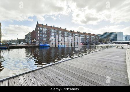 Amsterdam, pays-Bas - 10 avril 2021 : quelques bateaux dans l'eau et des bâtiments de l'autre côté de la rivière avec ciel nuageux au-dessus d'eux, comme vu de l'autre côté de la rivière Banque D'Images