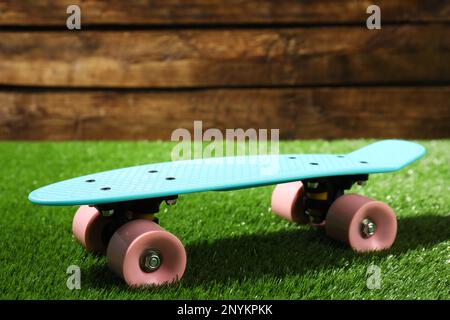 Planche à roulettes bleu clair avec roues roses sur herbe verte près d'un mur en bois Banque D'Images