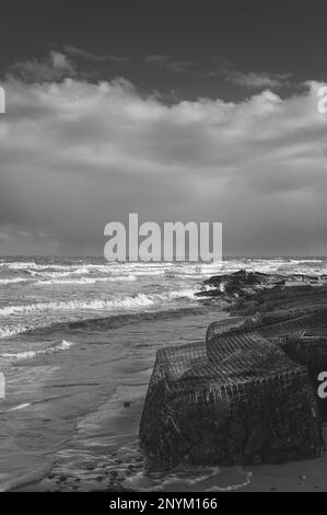 Panier de gabion avec des pierres sur une plage à Walton sur la Naze dans l'Essex. Froid, hiver, jour venteux. Les vagues s'écrasant contre le panier de gabion. Banque D'Images