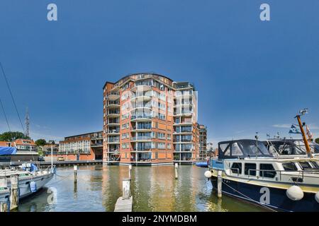 Amsterdam, pays-Bas - 10 avril 2021 : quelques bateaux amarrés dans l'eau près d'un grand bâtiment en briques avec plusieurs bals sur ses côtés et un complexe d'appartements derrière Banque D'Images