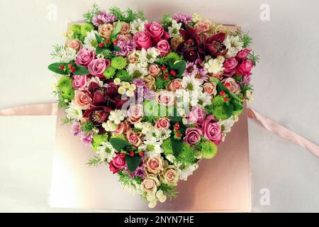 Un arrangement floral rose vif en forme de coeur sur une table, attaché avec art avec un ruban Banque D'Images