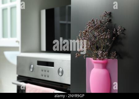 Vase en silicone avec de belles fleurs violettes au réfrigérateur dans la cuisine, espace pour le texte Banque D'Images