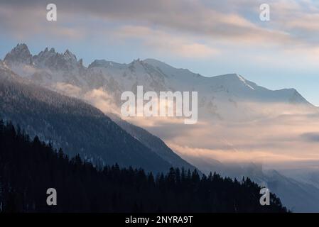 Couches de flanc de montagne formant des parties du massif du Mont blanc avec des feuilles de nuages au coucher du soleil d'hiver à Chamonix, en France Banque D'Images