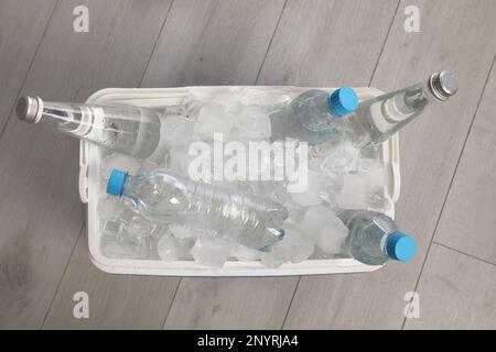 Glacière en plastique avec glaçons et bouteilles d'eau sur parquet, vue de dessus Banque D'Images