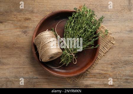 Bouquet de thym aromatique et ficelle dans un bol sur une table en bois, vue de dessus Banque D'Images