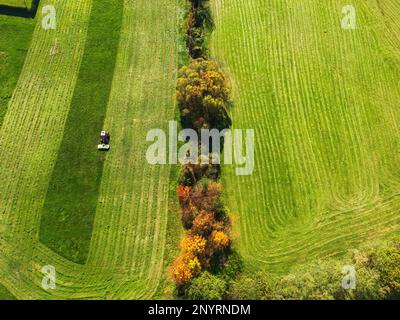 Vue aérienne d'un champ de gras vert fraîchement fauchée et d'un tracteur finissant de tondre un champ Banque D'Images